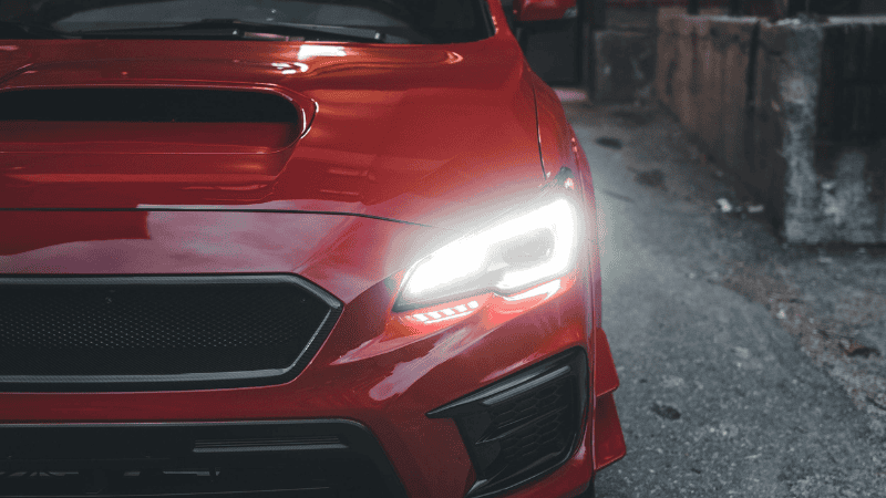 A red car with its headlights on.