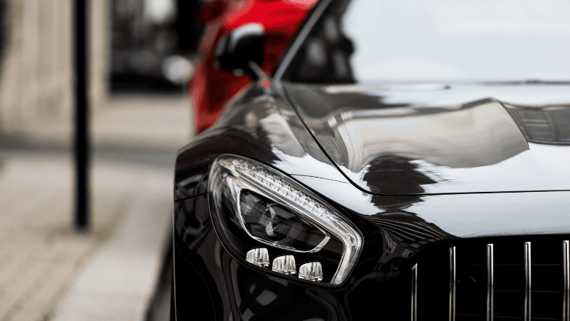 صورة مقربة لمصباح أمامي حديث بتقنية LED مضاء في مقدمة سيارة بيضاء، تُظهر تصميمه الأنيق وإضاءته الساطعة.