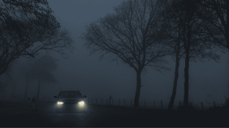 Vehicles on this dark road traveled by the faint light of headlights.