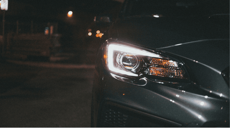 Vehicles with lights on at night are parked on the side of the road.