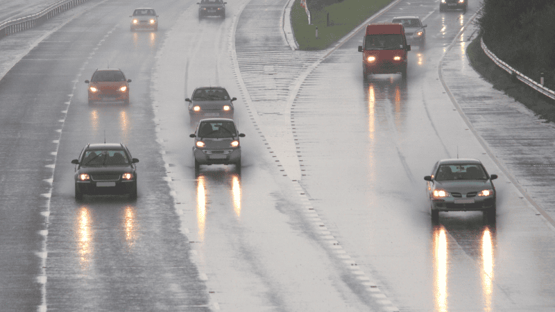 There are a lot of cars on the road with fog lights on a rainy day.