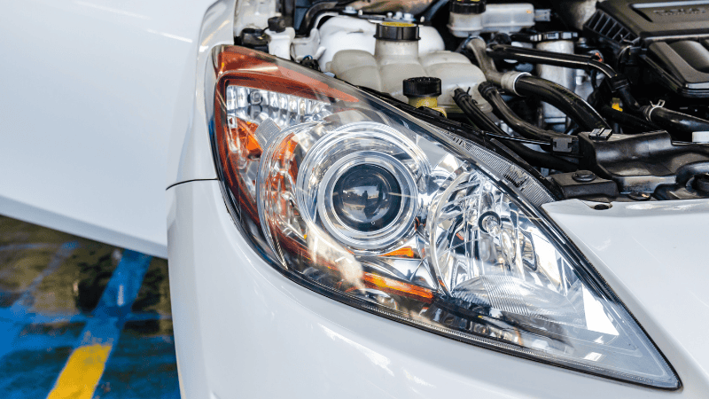 A mechanic in a garage installing new headlights on a modern car.